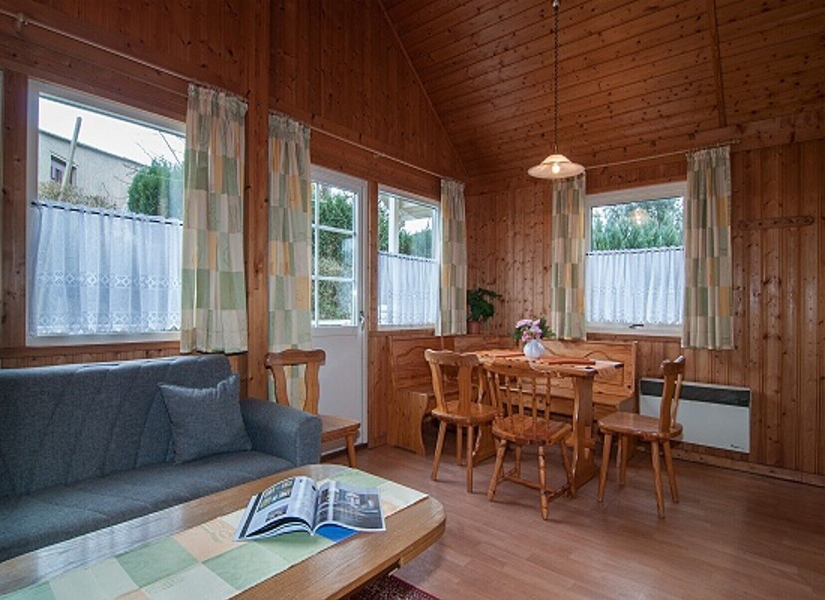 A cozy room with a wooden interior, a sofa, a dining table with chairs, and a window with curtains.