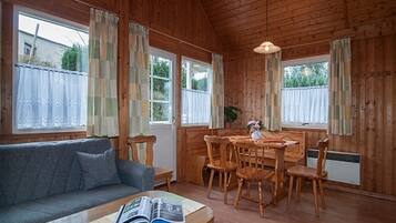 A cozy room with a wooden interior, a sofa, a dining table with chairs, and a window with curtains.