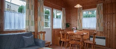 Una habitación acogedora con detalles de madera, un sofá, una mesa de comedor con sillas y una ventana con cortinas.