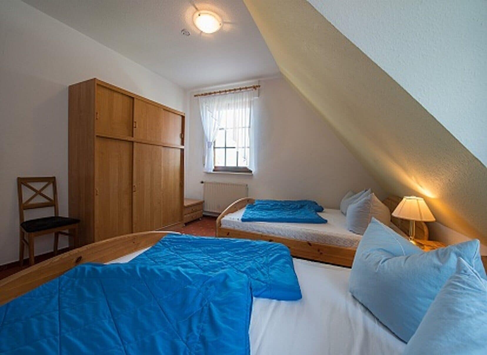 A bedroom with two beds, a wardrobe, a window with curtains, and a radiator.