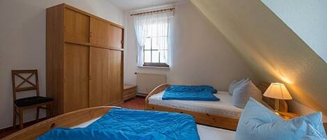 A bedroom with two beds, a wardrobe, a window with curtains, and a radiator.