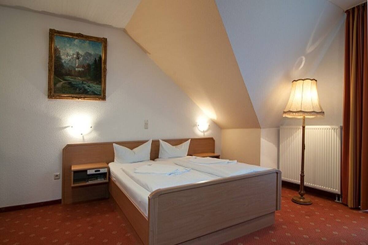Una habitació d'hotel amb un llit, una taula de nit, una làmpada, un quadre a la paret i un radiador.