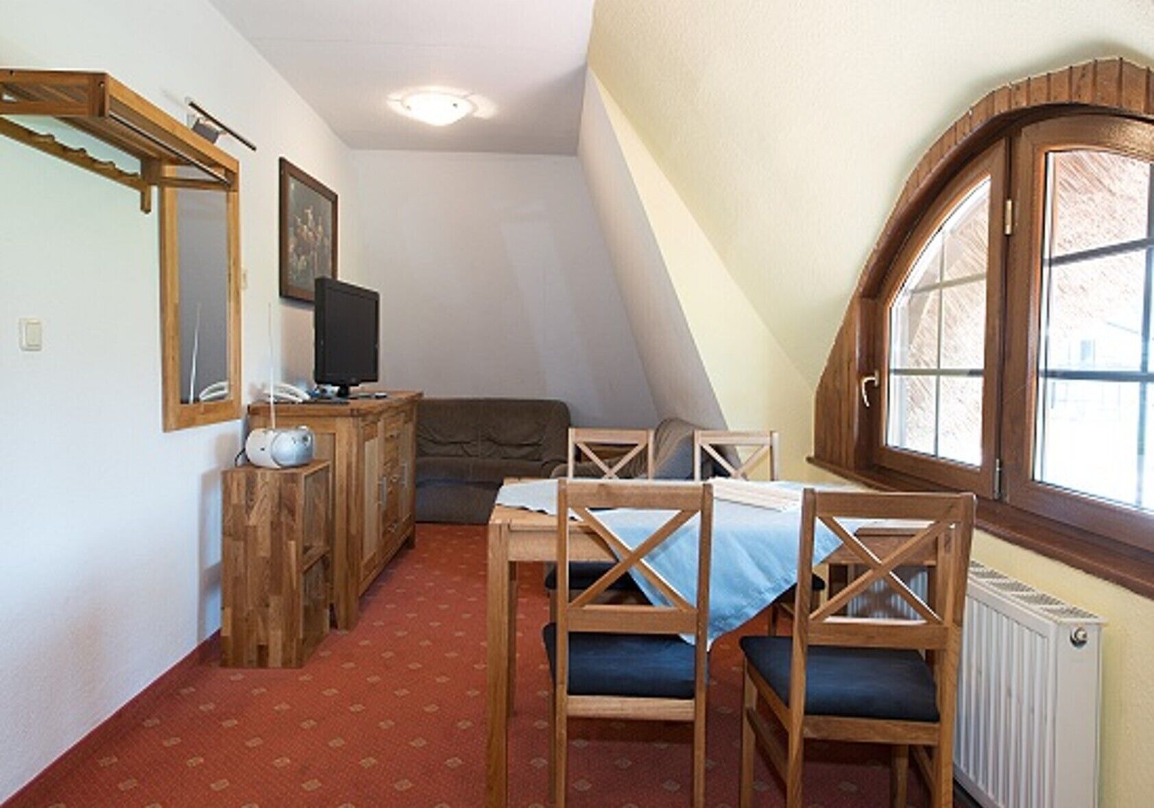 Una habitación pequeña y acogedora con un escritorio de madera, dos sillas, un sofá, un televisor y una ventana con marco de madera.
