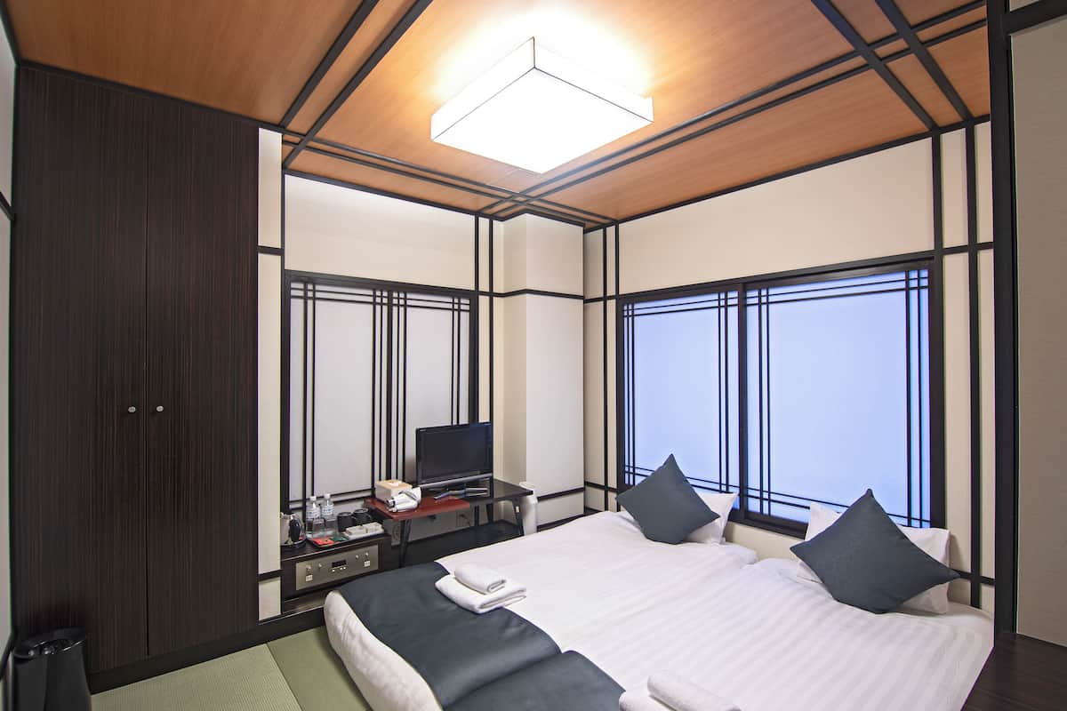 Quarto de hotel com uma cama grande, uma escrivaninha com computador, televisão e janela com vista.