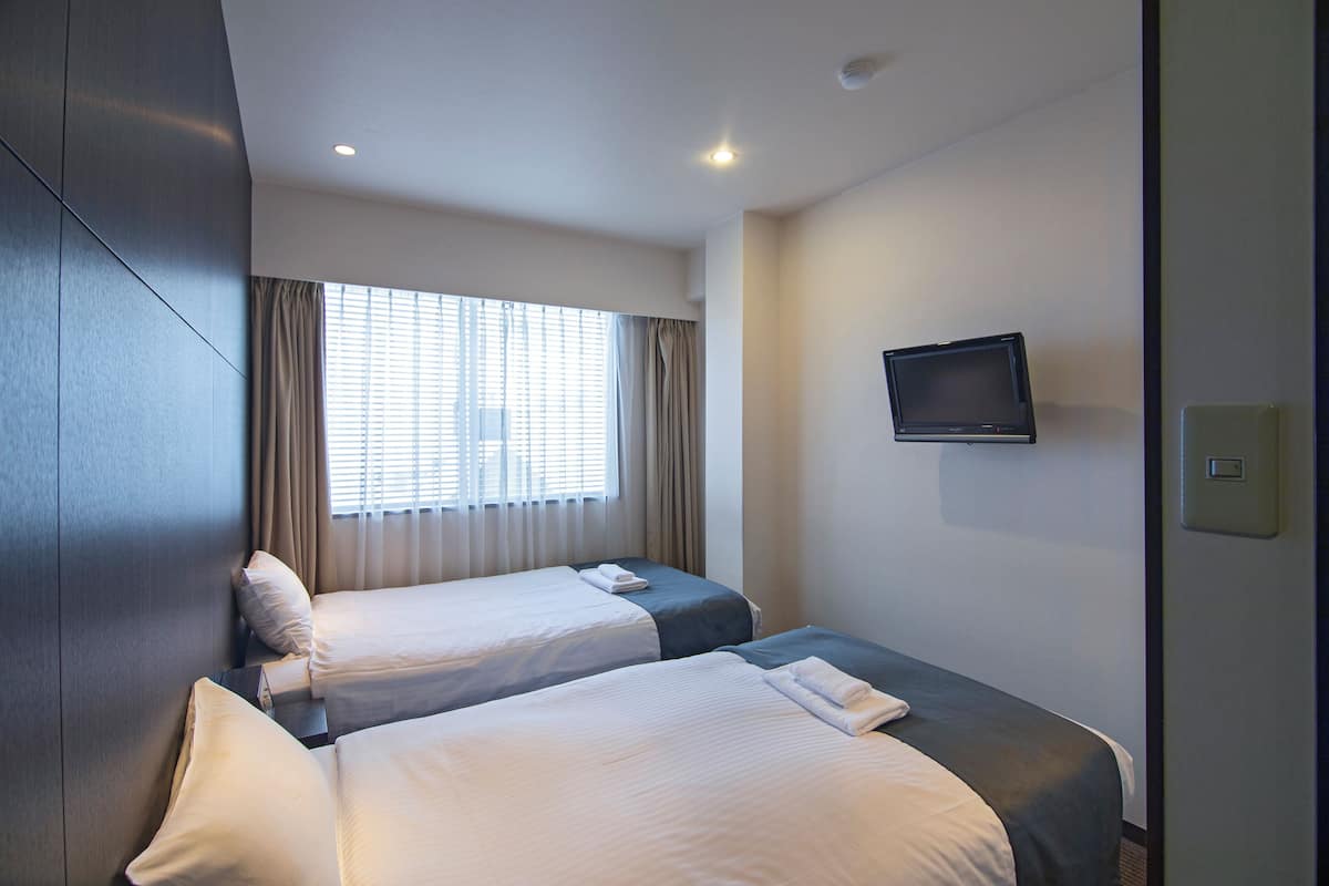 Quarto de hotel com duas camas, uma televisão na parede e uma janela com cortinas.