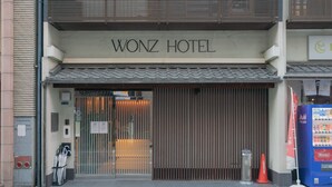 L’extérieur de l’hôtel Wonz présente une façade de style traditionnel, une entrée fermée par un portail et un distributeur automatique situé sur la droite.