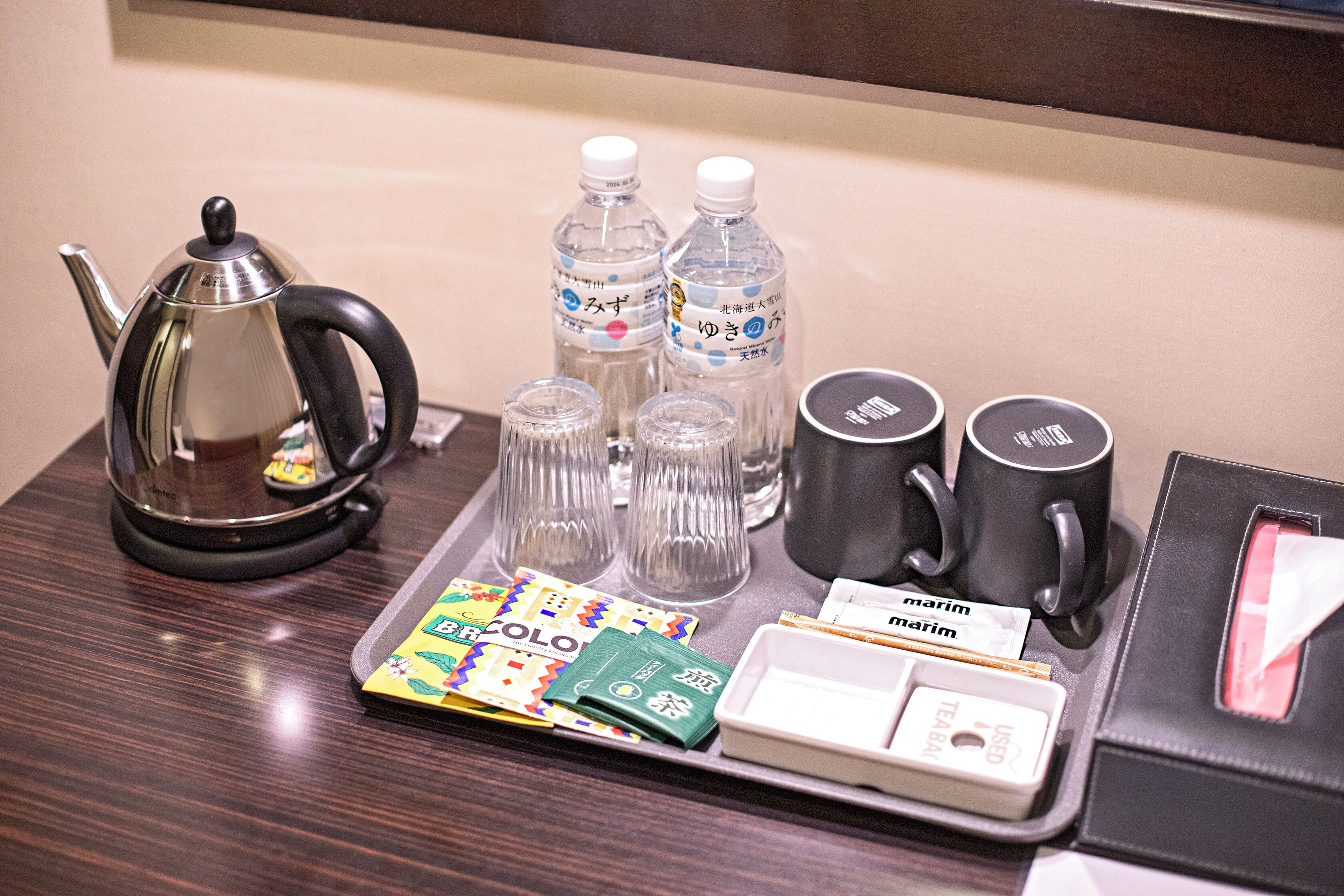 A tray with a teapot, water bottles, glasses, and a small box of tea bags.
