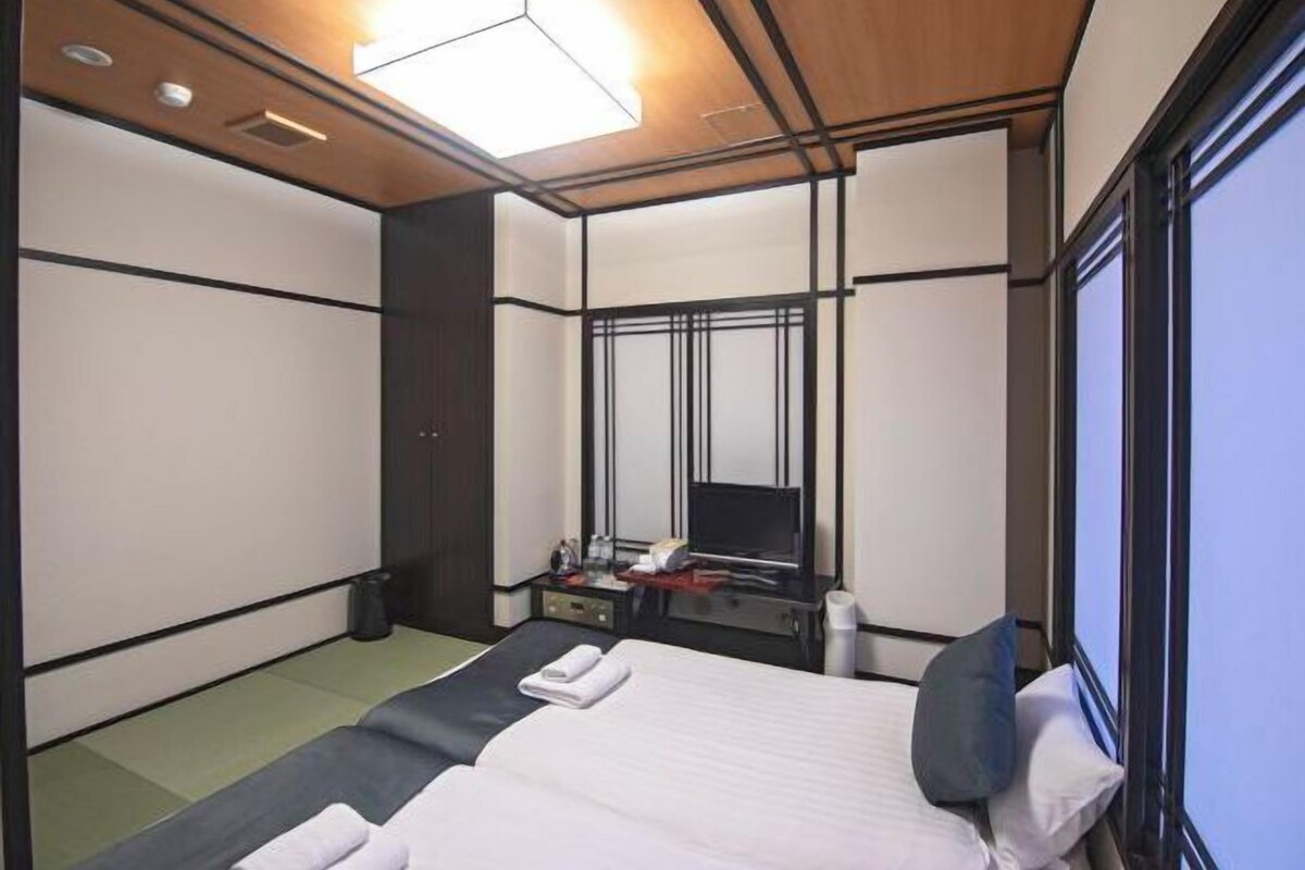 A hotel room with a bed, a desk with a flat-screen TV, a mirror, and a window.