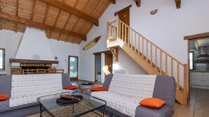 A cozy living room with a wooden staircase, a fireplace, and a dining area. - Belle Maison Landaise Prés des Plages (Tosse)