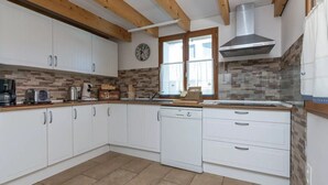 A kitchen with white cabinets, a wooden ceiling, a clock, and a window with curtains. - Belle Maison Landaise Prés des Plages (Tosse)