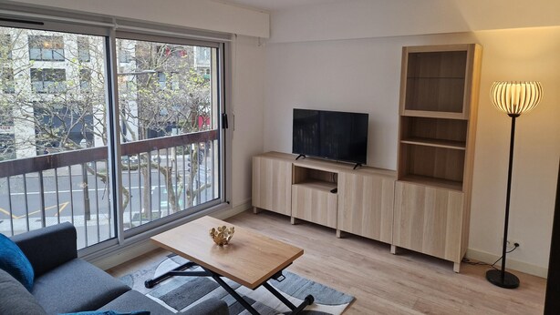 A modern living room with a sofa, a coffee table, a TV on a wooden cabinet, and a floor lamp. - À Louer Dans le Centre de Boulogne-billancourt à 10 mn en bus de Paris16éme (Boulogne-Billancourt)
