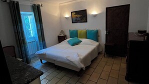 Une chambre à coucher comprenant un lit, une table de chevet, une lampe fixée au mur, une porte et une fenêtre avec des rideaux.