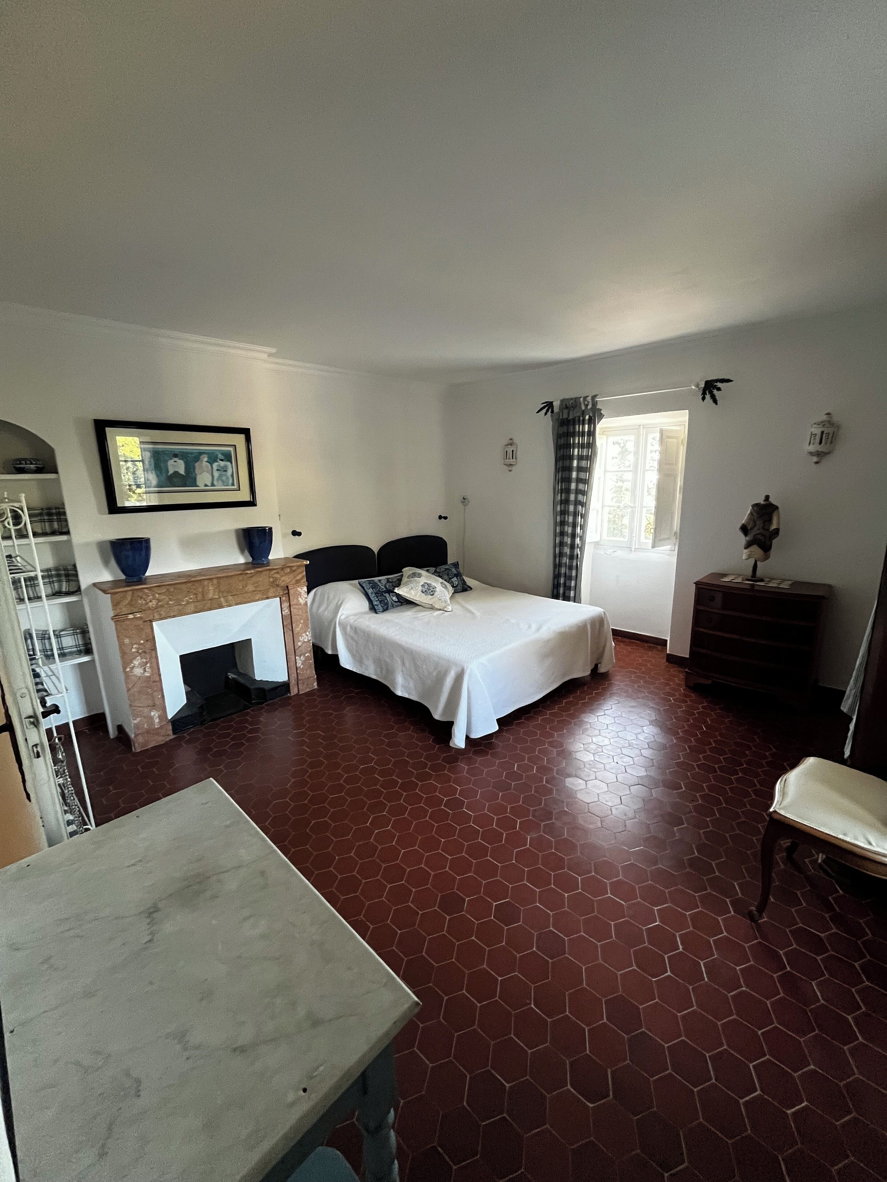 Un dormitorio con cama, escritorio, silla, chimenea y ventana con cortinas.