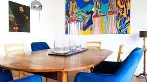 A dining area with a round wooden table, blue upholstered chairs, and a colorful abstract painting above. - 4-bed loft flat, station area - Angers (Angers)