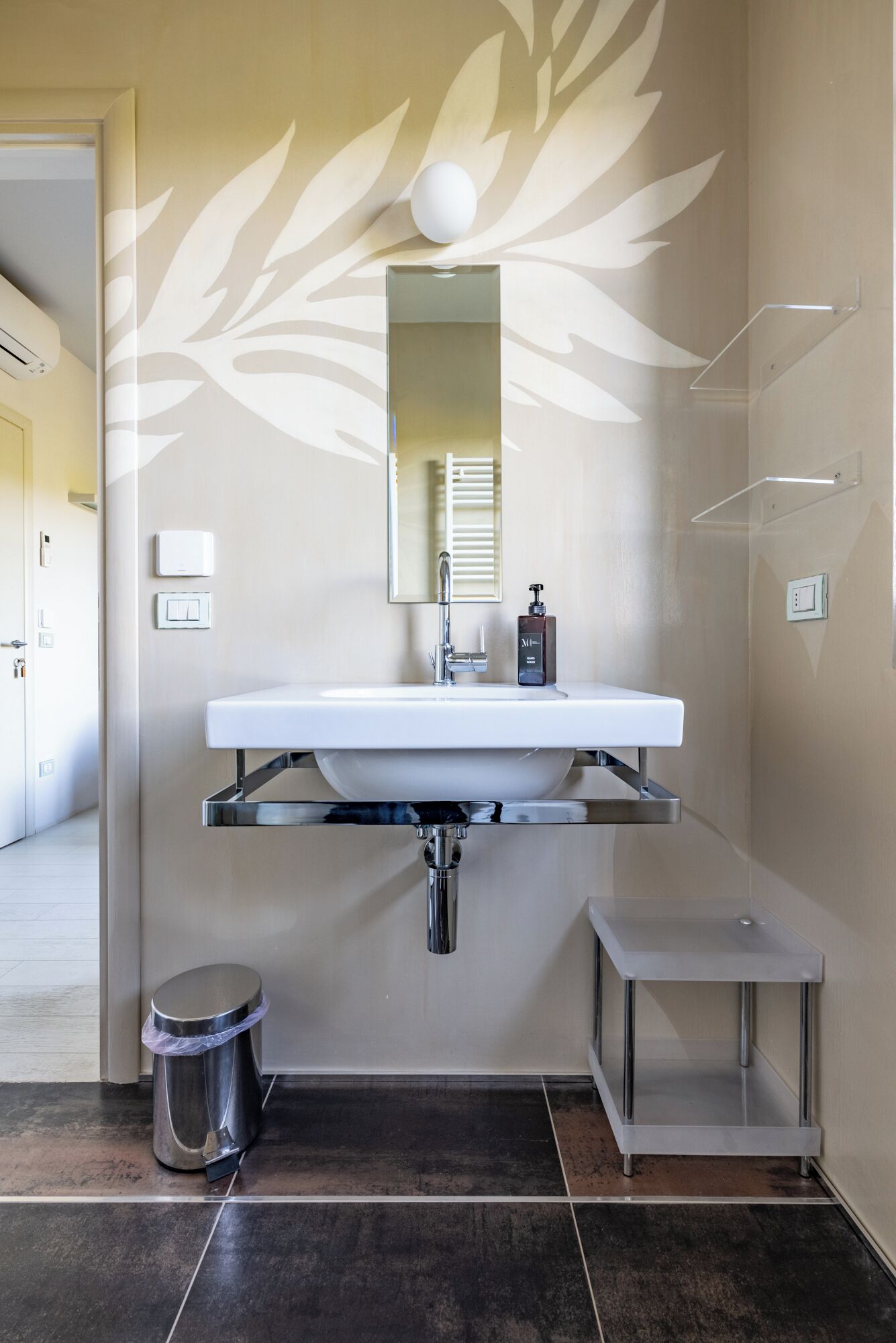 A modern bathroom with a large sink, a mirror, a towel rack, and a small trash bin.