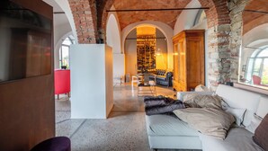 A spacious living area with a brick archway, a modern sofa, a red chair, and a wine rack in the background. - Tenuta Moncarlino (Morsasco)