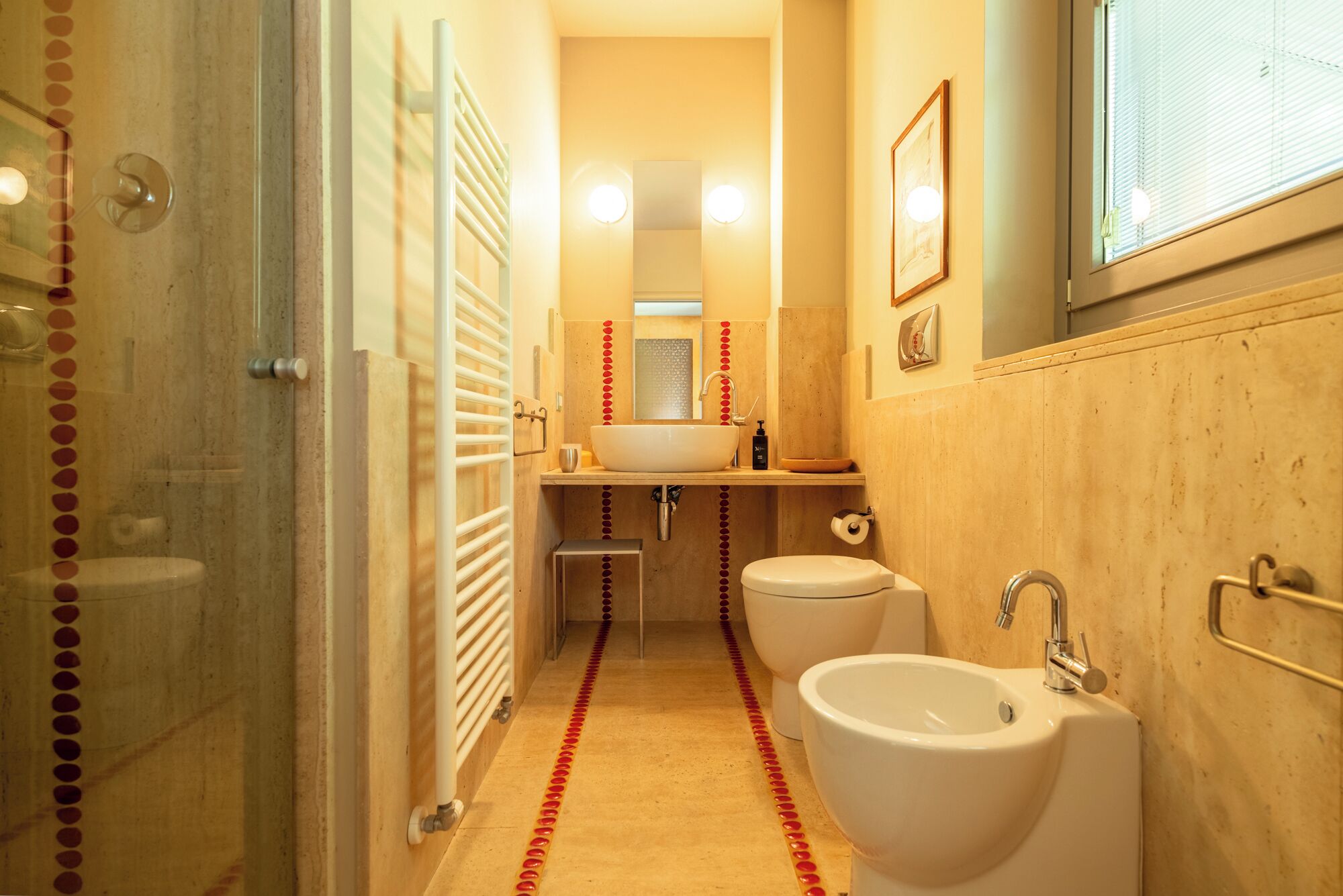 Un bagno stretto con una cabina doccia in vetro, un lavandino bianco, un WC e un bidet.