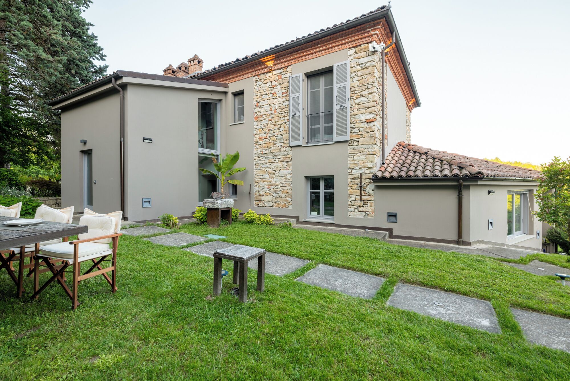 A modern house with a stone facade, a patio with a table and chairs, and a well-maintained lawn.