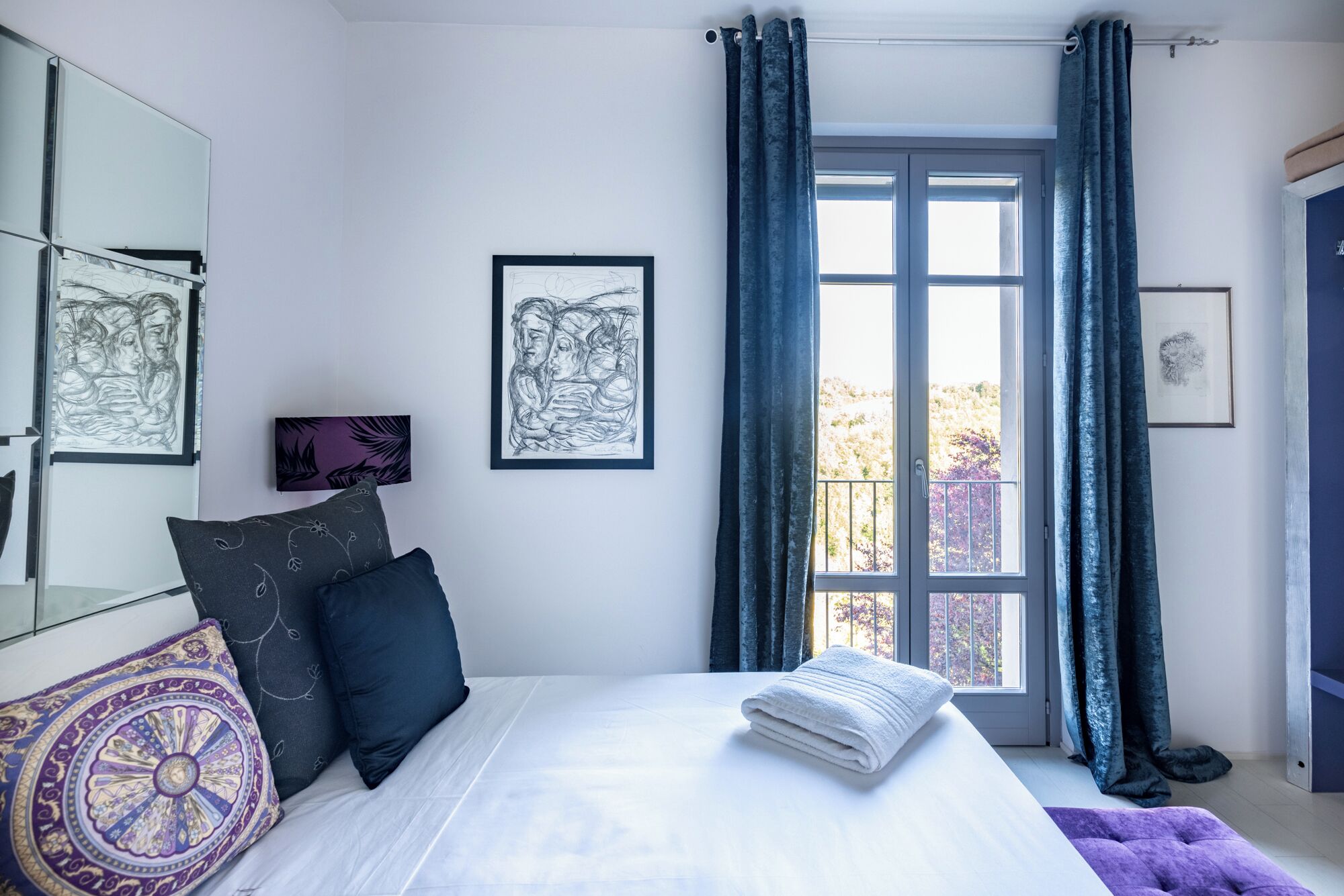 Ein Schlafzimmer mit Bett, einem Fenster mit Vorhängen und Kunstwerken an den Wänden.