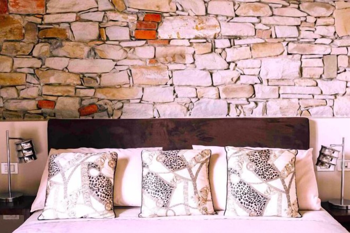 A bed with a stone wall backdrop, three patterned pillows, and a dark headboard.