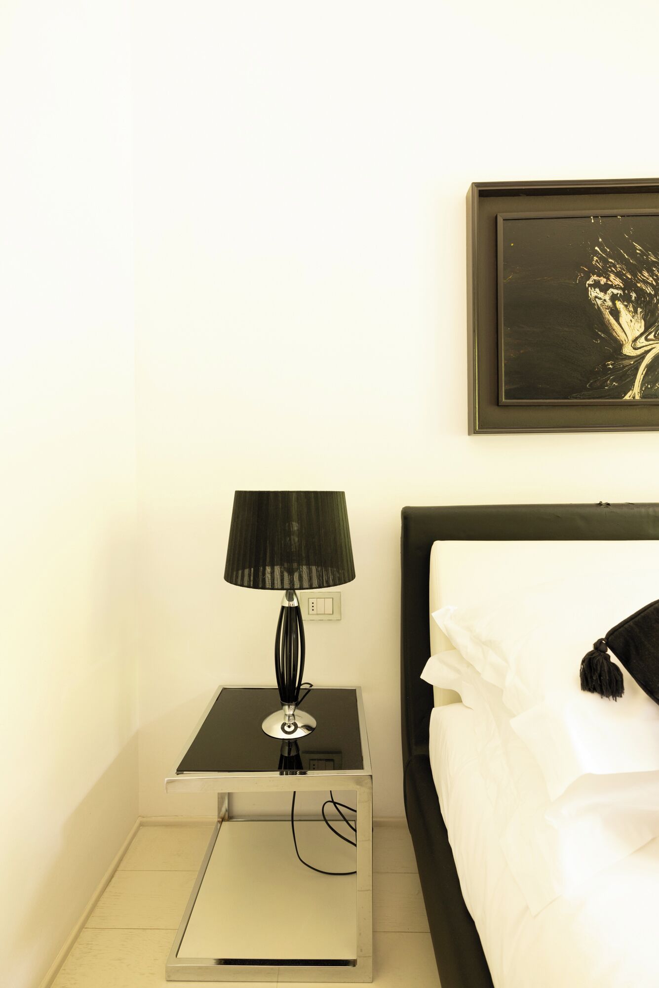 Ein Hotelzimmer mit einem Bett, einem Nachttisch mit Lampe, einer Steckdose und einem gerahmten Kunstwerk an der Wand.