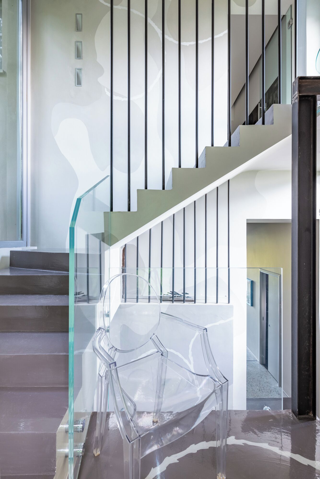 Un escalier moderne avec des rampes en verre et une chaise en plastique transparent au premier plan.