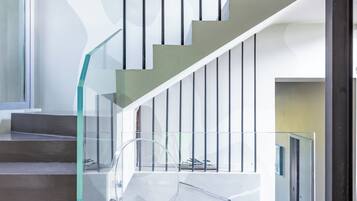 Un escalier moderne avec des rampes en verre et une chaise en plastique transparent au premier plan.