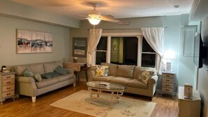 A living room with two sofas, a coffee table, a ceiling fan, and a window with curtains. - Charming Falmouth Heights Steps to Beach (Falmouth)