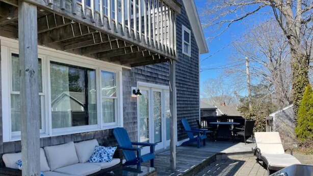 A covered outdoor seating area with a sofa and chairs, a grill, and a small table. - Charming Falmouth Heights Steps to Beach (Falmouth)