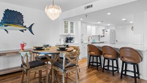 A modern kitchen with white cabinetry, a dining area with wooden chairs, and a large fish mural on the wall. - SD 406: The Beachcomber - Where Every Sunset Feels Like a New Beginning! (Fort Walton Beach)