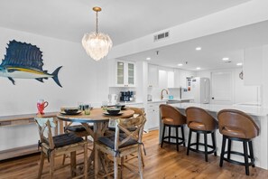A modern kitchen with white cabinetry, a dining area with wooden chairs, and a large fish mural on the wall.