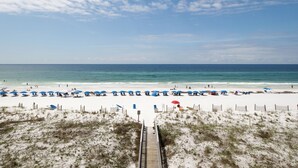 A beach with a wooden boardwalk leading to the shore, white sand, and blue umbrellas. - SD 406: The Beachcomber - Where Every Sunset Feels Like a New Beginning! (Fort Walton Beach)