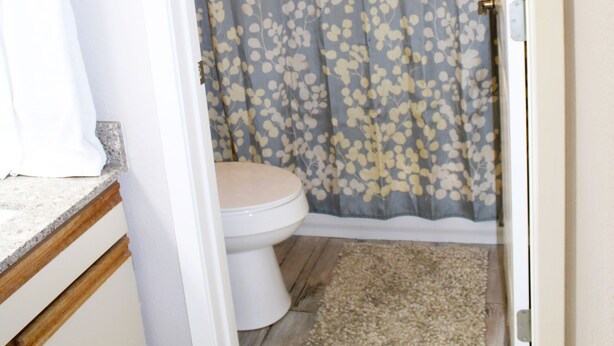 Ein Badezimmer mit Toilette, Duschvorhang und einem beigen Teppich.