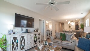 A living room with a TV, a sofa, a coffee table, and a dining area in the background.