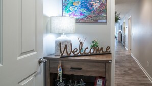 A hallway with a welcome sign, a lamp, and a colorful abstract painting on the wall.