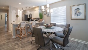 A modern kitchen with white cabinets, a central island, and a dining area with a round table and chairs.