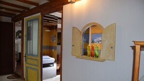 A room with a wooden door leading to another room, a window with a view of a snowy landscape, and a shelf with colorful bottles. - Authentic charm in Corbas: 120m² of comfort (Corbas)
