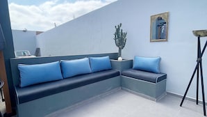 Eine Sitzecke mit blauer Couch und Kissen, einem kleinen Tisch mit einem Kaktus und einer Stehlampe.