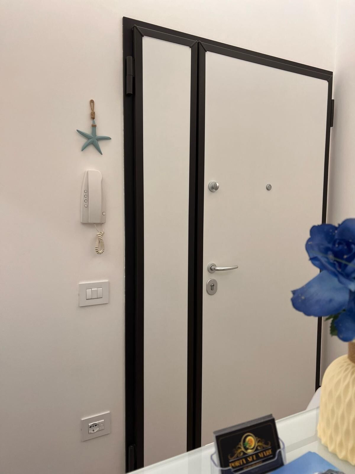 A door with a black frame, a starfish decoration, a phone, a light switch, and a blue flower.