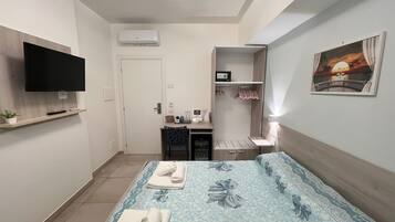 A hotel room with a bed, a TV, a desk, a wardrobe, and a painting on the wall.