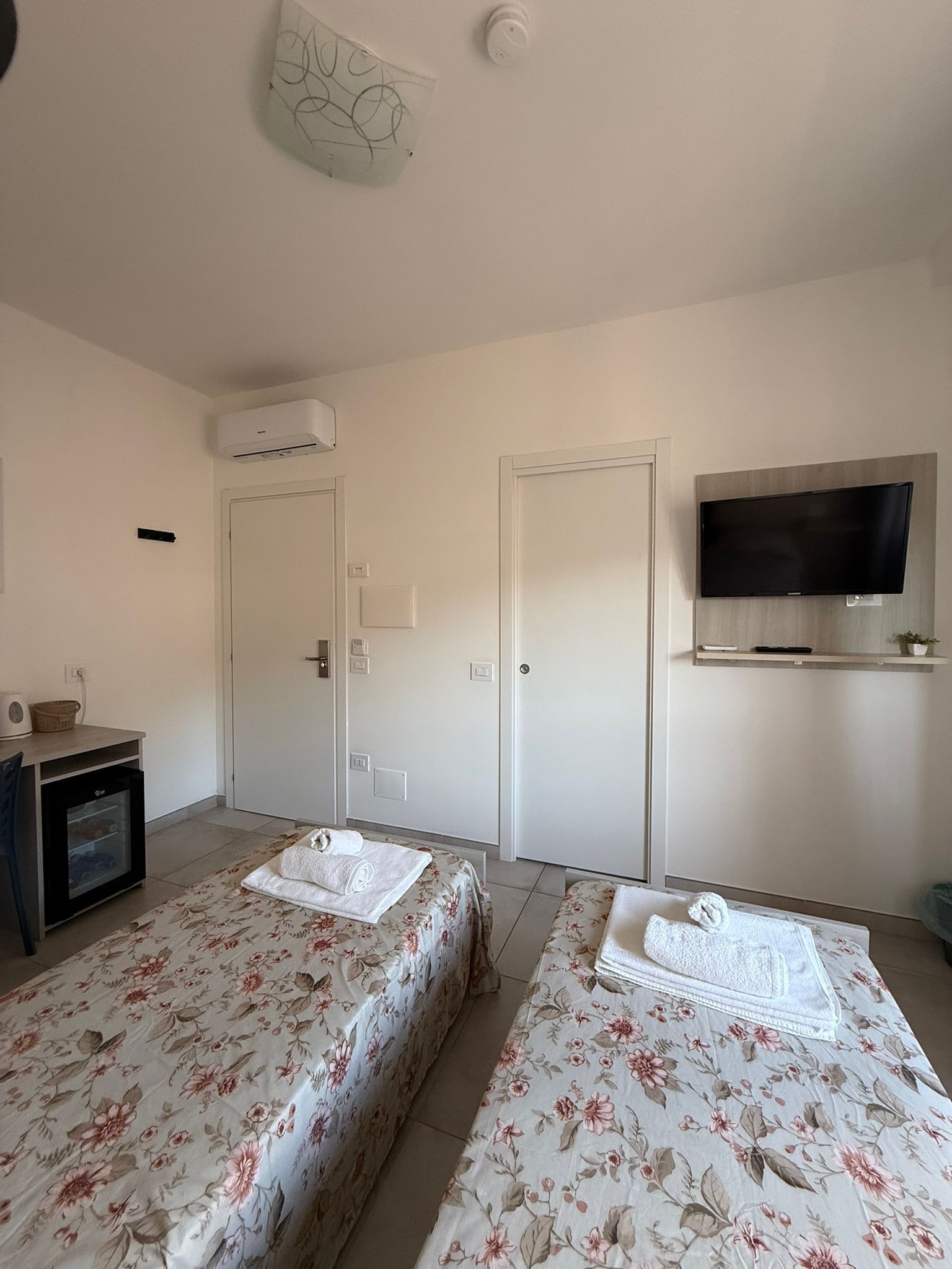 Et hotelværelse med to senge, et fjernsyn, et lille tekøkken og en loftsvifte.