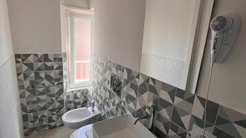 Un baño moderno con un salpicadero de azulejos geométricos, un espejo grande, un secador de pelo montado en la pared y una ventana que proporciona luz natural.