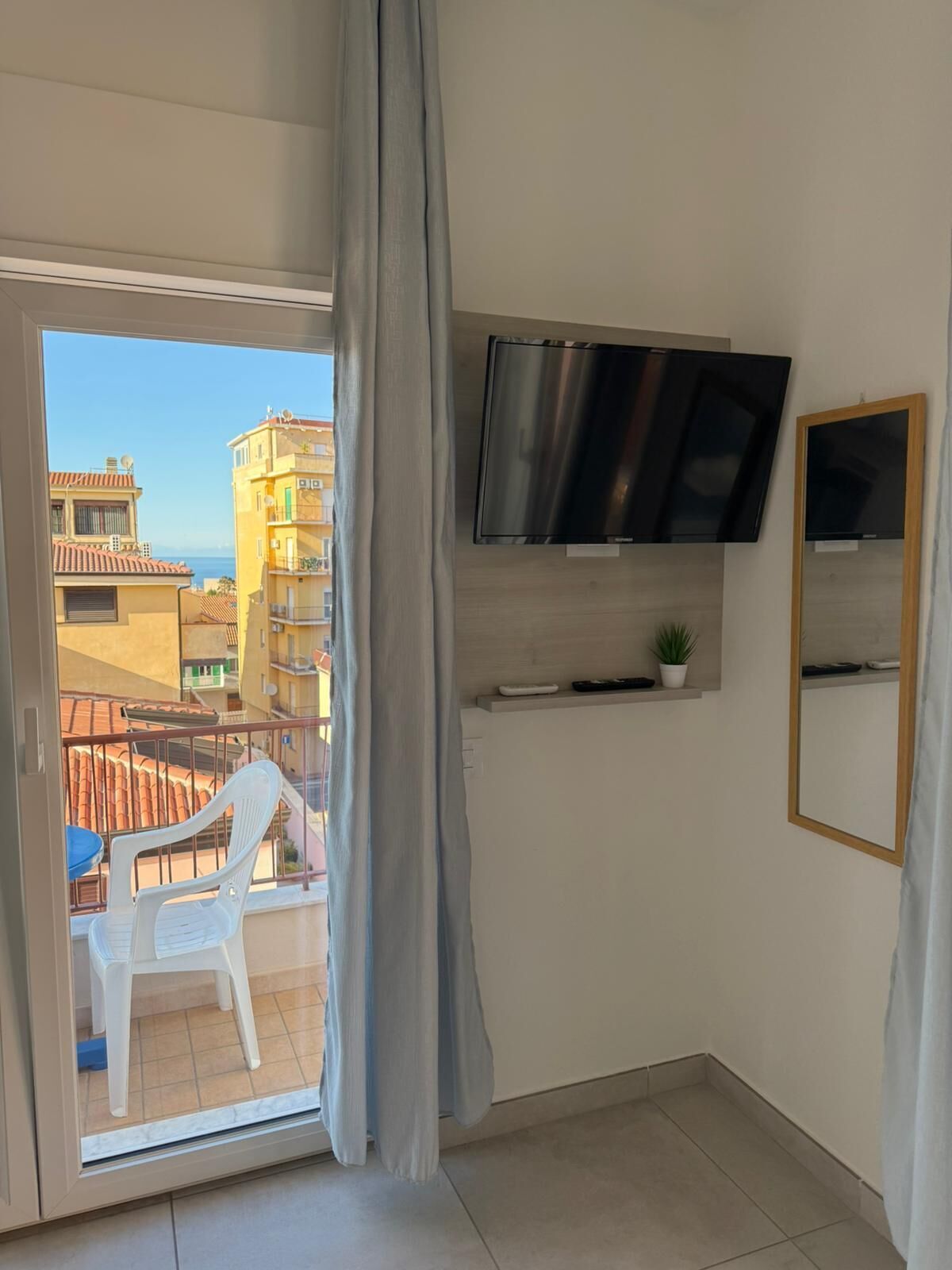 A balcony with a white plastic chair, a TV mounted on the wall, and a potted plant.