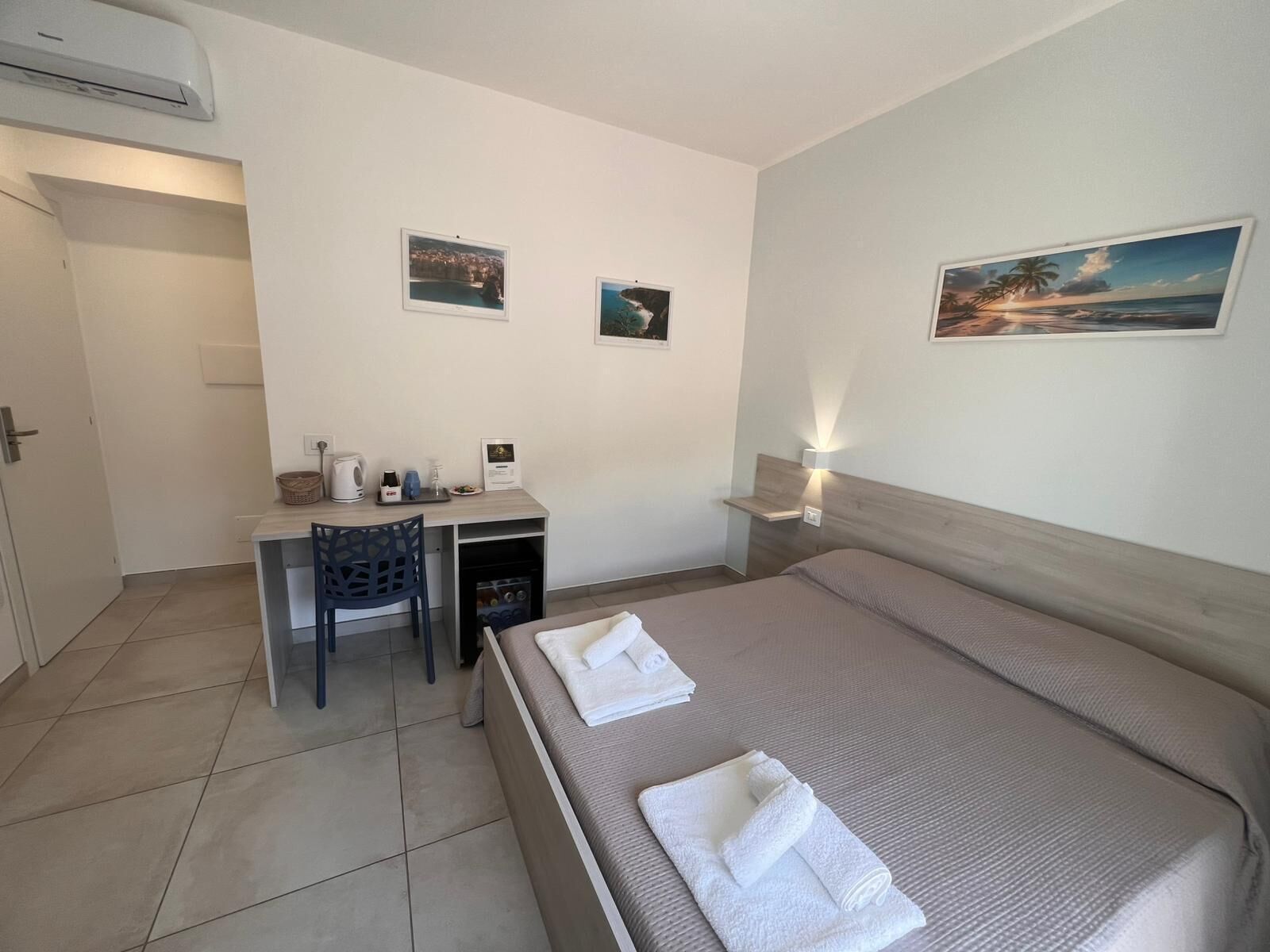 Ein Hotelzimmer mit einem Bett, einem Schreibtisch, einem Sessel, einem kleinen Tisch und zwei Wandbildern.