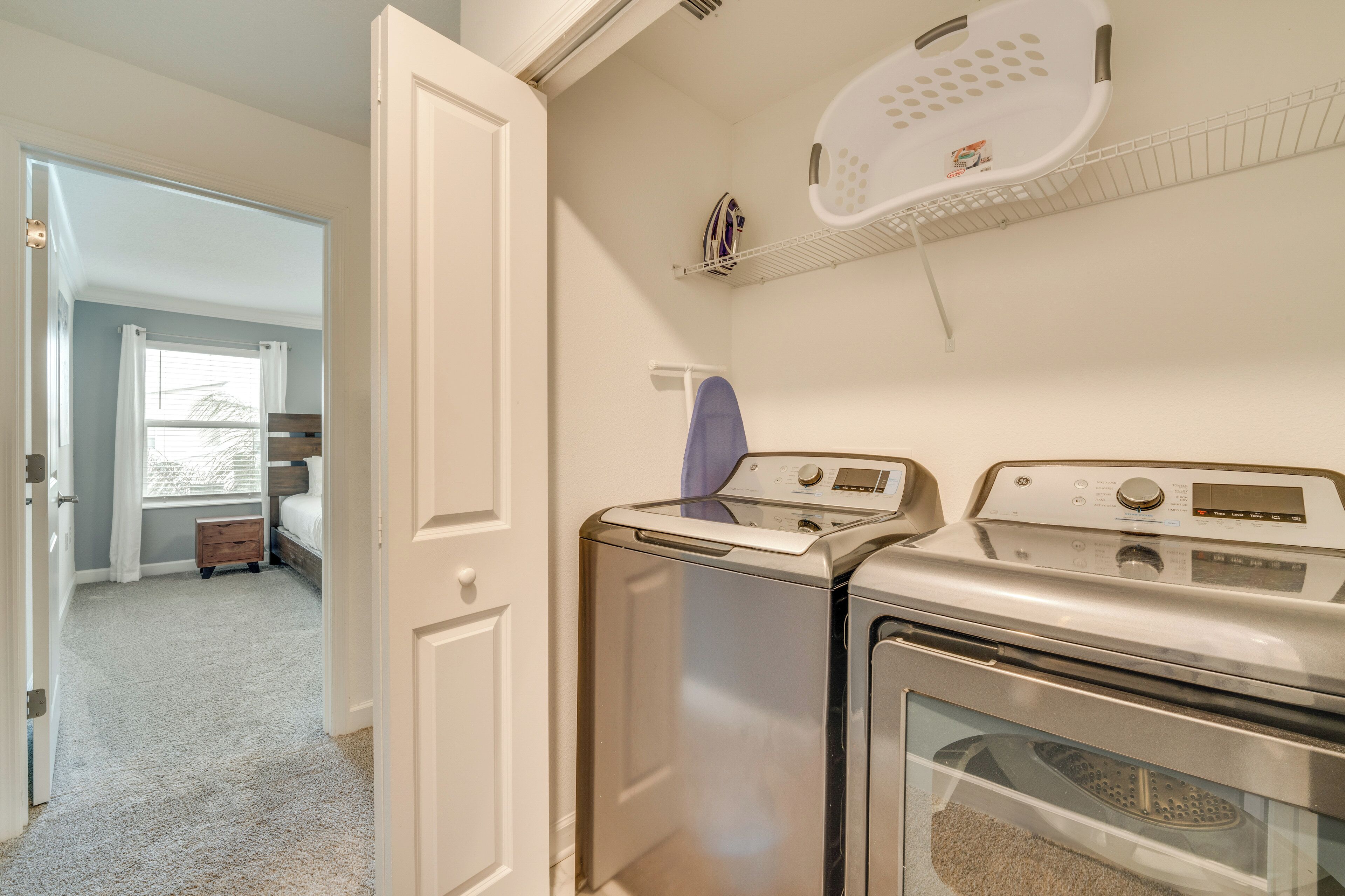 A laundry room with a front-loading washer and dryer, a drying rack, and a small wooden cabinet.