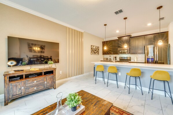 A modern kitchen with a bar area, a dining table, and a large flat-screen TV.