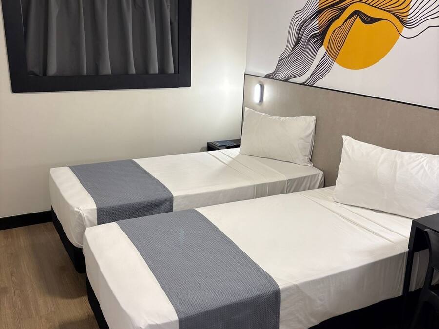 Une chambre d’hôtel avec deux lits simples, une grande peinture abstraite au mur, une fenêtre avec des rideaux et un plancher en bois.