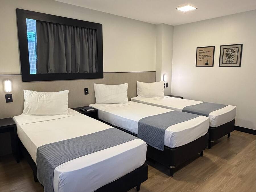 Habitación de hotel con cuatro camas, un televisor de pantalla plana y un ventanal grande con cortinas.