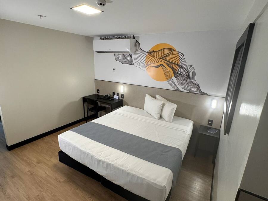 A modern hotel room with a large bed, a desk, and a wall-mounted air conditioner.