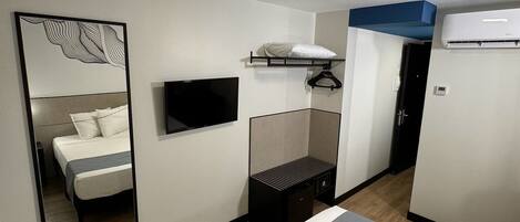 Habitación de hotel moderna con cama, televisor de pantalla plana, espejo, armario y unidad de aire acondicionado.